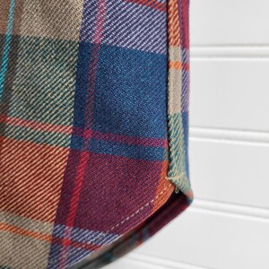 Peut inclure: Gros plan sur un tissu &agrave; carreaux dans les tons de turquoise, bleu, rouge, violet, beige et orange. Le tissu a une texture tiss&eacute;e et fait probablement partie d'une chemise ou d'un autre v&ecirc;tement.