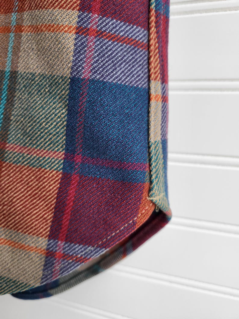 Peut inclure: Gros plan sur un tissu &agrave; carreaux dans les tons de turquoise, bleu, rouge, violet, beige et orange. Le tissu a une texture tiss&eacute;e et fait probablement partie d'une chemise ou d'un autre v&ecirc;tement.