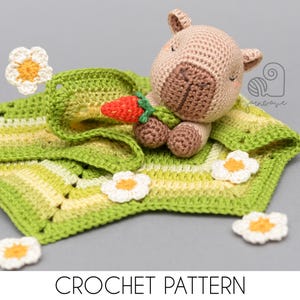 Peut inclure: Un jouet hippopotame crocheté avec une carotte, posé sur une couverture verte et jaune, entouré de fleurs crochetées blanches et jaunes. L'image comprend le texte "CROCHET PATTERN".