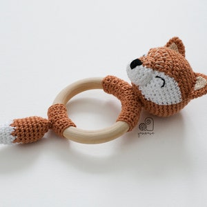May include: A crocheted fox rattle with a wooden ring. The fox is brown and white with a smiling face. The rattle is perfect for babies and toddlers.