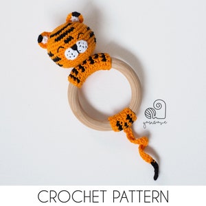 May include: A crocheted tiger rattle toy with a wooden ring. The tiger is orange and black with a white face and black eyes. The toy is perfect for babies and toddlers.