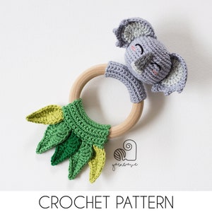 May include: A crocheted elephant rattle with a wooden ring and green leaves. The elephant has a gray and white color scheme with pink cheeks. The rattle is a great toy for babies and toddlers.