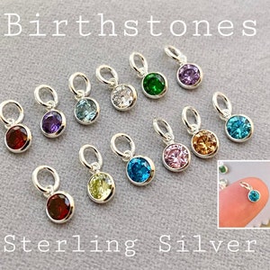 May include: A collection of sterling silver birthstone pendants with various colored gemstones. The pendants are round with a small loop at the top. The image includes the text "Birthstones" and "Sterling Silver".
