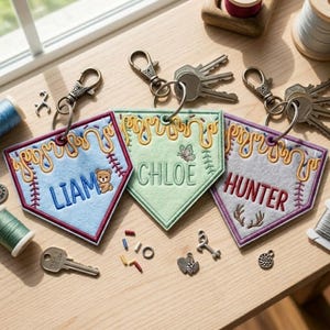 May include: Three pentagonal felt keychains with metal lobster clasps. The light blue one features the name LIAM and a teddy bear. The light green one features the name CHLOE and a butterfly. The gray one features the name HUNTER and antlers.