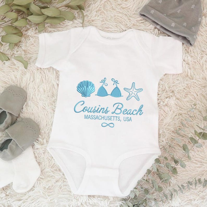 Puede incluir: Body de beb&eacute; blanco con gr&aacute;ficos azules de concha, top de bikini y estrella de mar. El texto dice "Cousins Beach, Massachusetts, USA" con un s&iacute;mbolo de infinito. Incluye zapatos de beb&eacute; y un gorro gris.