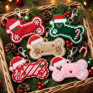 Può includere: Cinque portachiavi a forma di osso con moschettoni in metallo, ognuno decorato con un cappello da Babbo Natale ricamato. I motivi includono rosso con fiocchi di neve, verde con bastoncino di zucchero, beige con impronte, righe e rosa chiaro.