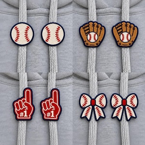 May include: Four sets of two matching embroidered drawstring charms attached to gray hoodie strings. The designs include white baseballs with red stitching, brown baseball gloves with white balls, red foam fingers with white #1 text, and white bows with red stitching.