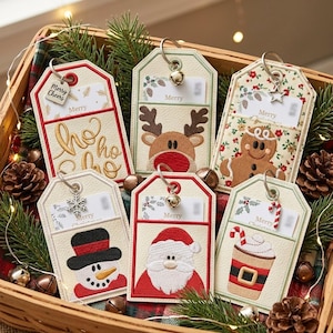 May include: Six rectangular gift tags with pockets, each featuring embroidered holiday designs including a snowman, Santa, reindeer, gingerbread person, and a cocoa cup. Each tag has a metal ring with a charm and a card labeled Merry.
