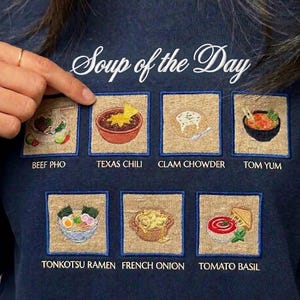 Puede incluir: Sudadera azul marino con diseño bordado "Soup of the Day". Presenta seis parches cuadrados con ilustraciones detalladas de varias sopas: Beef Pho, Texas Chili, Clam Chowder, Tom Yum, Tonkotsu Ramen, French Onion y Tomato Basil.