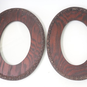 May include: Two antique oval picture frames. The frames are made of dark wood with a reddish-brown stain and a decorative floral border. The frames have an oval opening in the center.