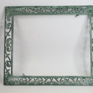 May include: A square metal frame featuring a weathered green patina finish. The border displays an intricate openwork design composed of repeating leaf and vine motifs, creating a decorative structure with a hollow center and a textured surface.