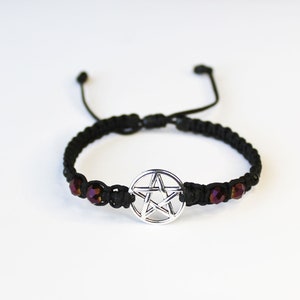 May include: Black braided bracelet with a silver pentagram charm and iridescent purple beads.