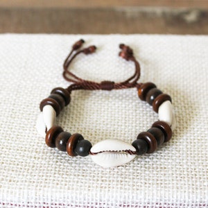 May include: A brown and white beaded bracelet with a brown cord closure. The bracelet features white shell beads and brown wooden beads.