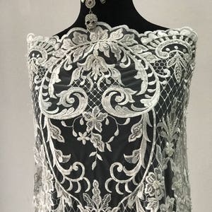 May include: White lace fabric with a floral pattern and pearl embellishments. The lace is delicate and intricate, and the pearls add a touch of elegance.