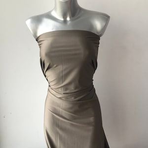 Può includere: Un tessuto liscio di colore marrone drappeggiato su un manichino. Il tessuto è piegato e disposto su una superficie bianca.