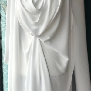 Op de afbeelding: Witte stof gedrapeerd over een mannequin, wat de gladde textuur en de vloeiende drape laat zien. De stof is kreukvrij en heeft een zacht, zijdeachtig gevoel.