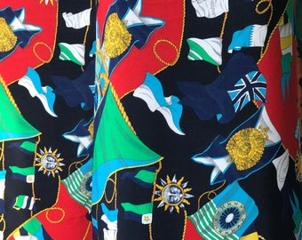 May include: Fabric with a repeating pattern of flags, suns, and decorative emblems in red, black, blue, green, and white. The flags include various designs, some with gold rope accents.