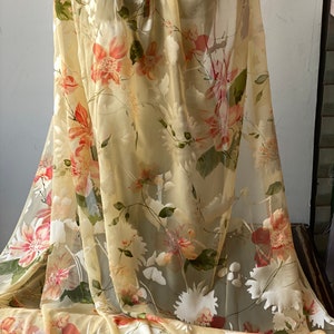 May include: A sheer fabric with a floral print in shades of yellow, orange, and green. The fabric is lightweight and translucent, making it ideal for creating garments or home decor.