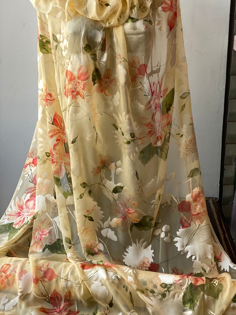 May include: A sheer fabric with a floral print in shades of yellow, orange, and green. The fabric is lightweight and translucent, making it ideal for creating garments or home decor.