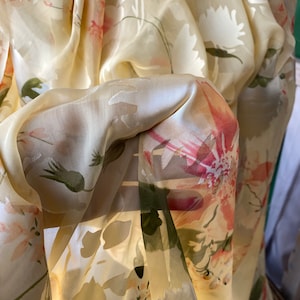 May include: A sheer, yellow fabric with a floral pattern. The fabric is draped and folded, creating a soft and delicate look.