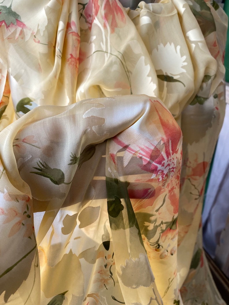 May include: A sheer, yellow fabric with a floral pattern. The fabric is draped and folded, creating a soft and delicate look.