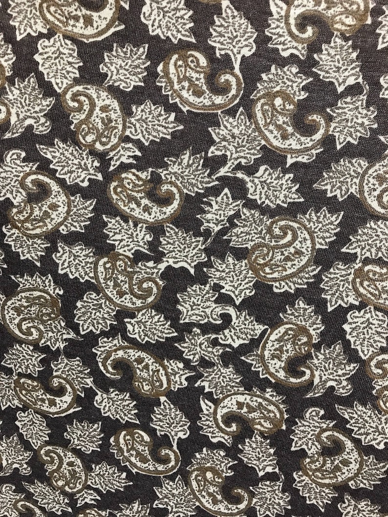 May include: A dark brown fabric with a white paisley pattern. The pattern features intricate swirls and leaves.