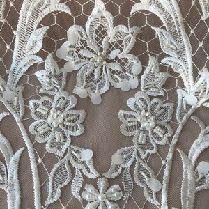 May include: White lace fabric with floral embroidery and pearl and sequin embellishments.