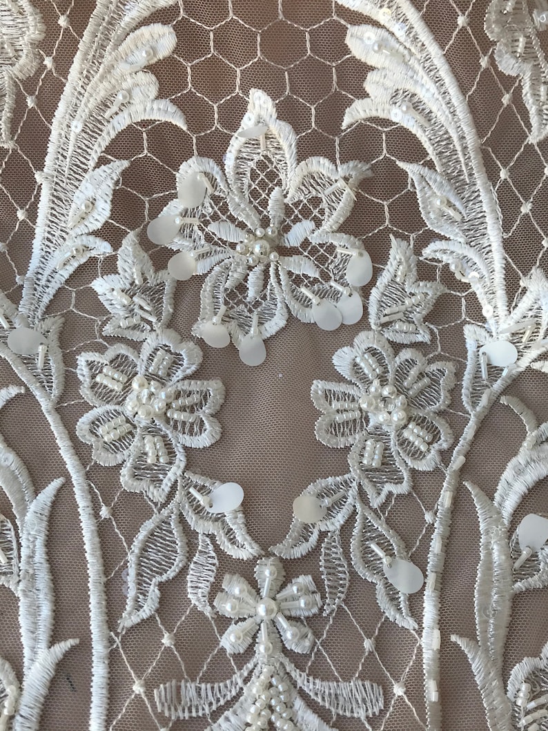 May include: White lace fabric with floral embroidery and pearl and sequin embellishments.