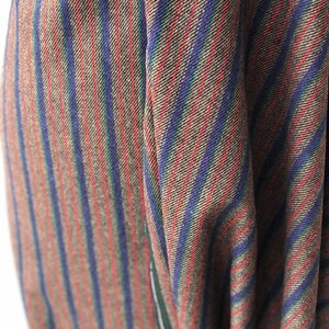 May include: Close-up of a brown, blue, red, and green striped fabric. The fabric has a woven texture and is folded in a way that shows the stripes.