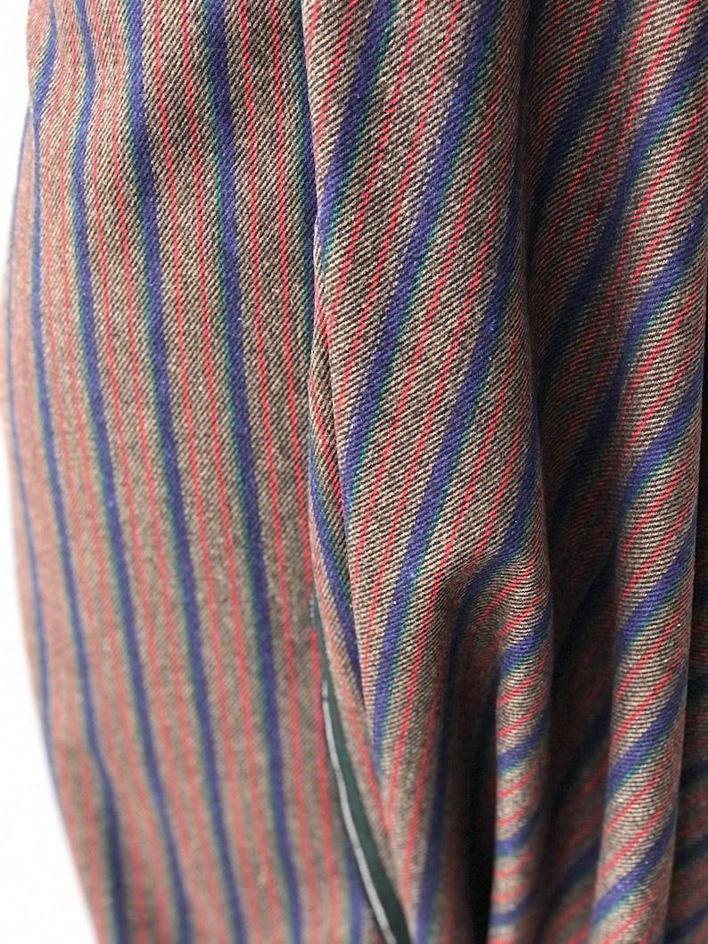 May include: Close-up of a brown, blue, red, and green striped fabric. The fabric has a woven texture and is folded in a way that shows the stripes.