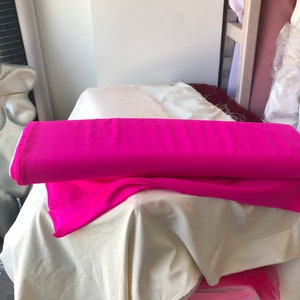 May include: A roll of bright pink fabric folded on top of a white fabric. The fabric is on a table with a white surface.