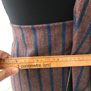 May include: Close-up of a brown, blue, and red striped fabric with a ruler measuring 35 centimeters. The fabric has a subtle herringbone pattern.