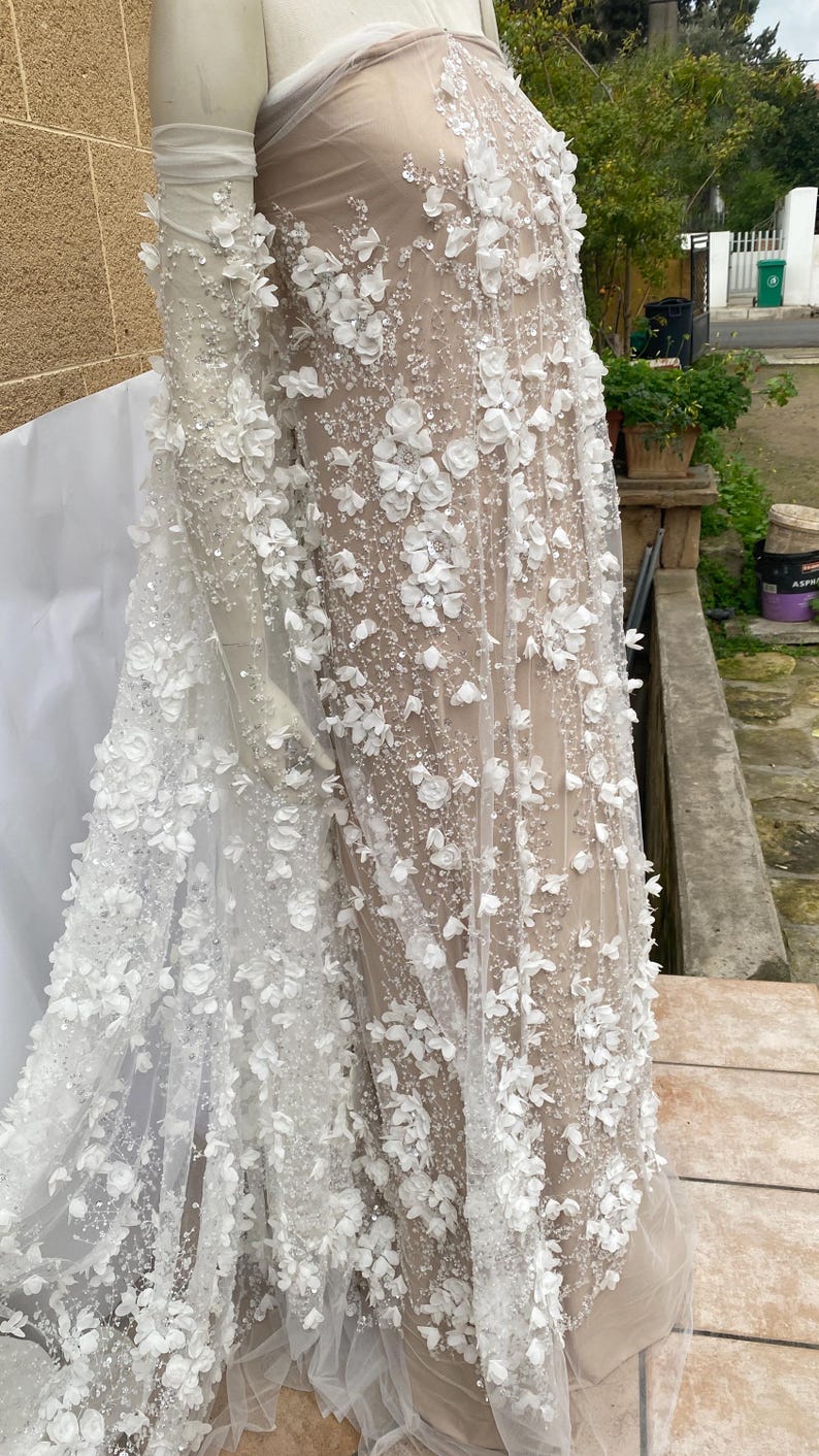Peut inclure: Tissu de tulle blanc avec des embellissements floraux 3D. Le tissu est transparent et a un aspect d&eacute;licat et f&eacute;minin.