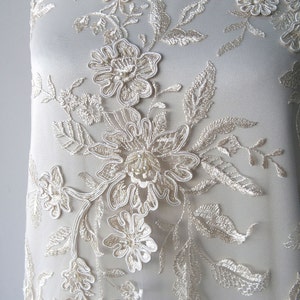 May include: Ivory lace fabric with a floral design. The flowers are 3D and have a beaded center. The fabric is sheer and delicate.