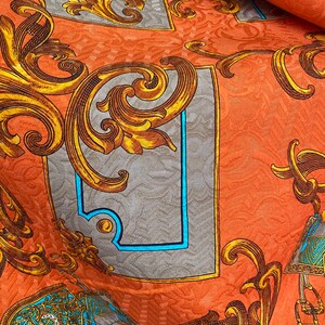 K&ouml;nnte beinhalten: Orangener Stoff mit einem goldenen und blauen Barockmuster. Der Stoff zeigt komplizierte florale Designs und verzierte Rahmen.