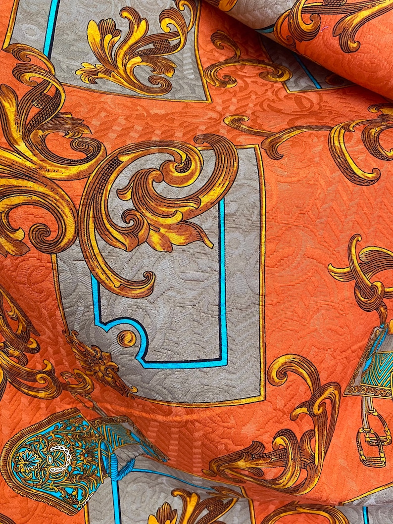 K&ouml;nnte beinhalten: Orangener Stoff mit einem goldenen und blauen Barockmuster. Der Stoff zeigt komplizierte florale Designs und verzierte Rahmen.