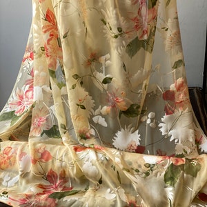 May include: A sheer fabric with a floral print in shades of yellow, white, and pink. The fabric is lightweight and translucent, making it ideal for curtains, scarves, or other decorative projects.