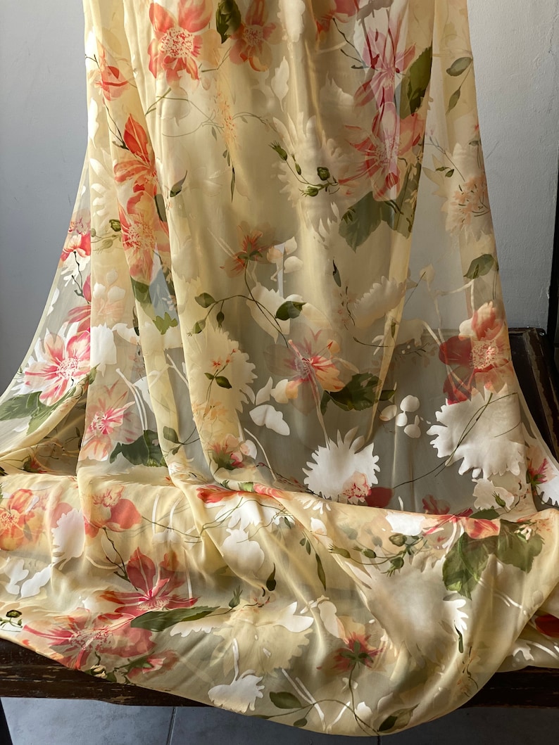 May include: A sheer fabric with a floral print in shades of yellow, white, and pink. The fabric is lightweight and translucent, making it ideal for curtains, scarves, or other decorative projects.