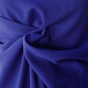 Puede incluir: Primer plano de una tela azul oscuro con una superficie suave y texturizada. La tela está doblada y drapeada, creando un aspecto suave y fluido.