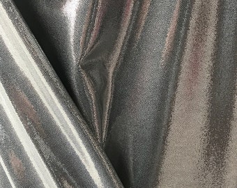 May include: Close-up of a silver fabric with a textured, dotted pattern. The material is folded, creating shadows and highlights that emphasise its reflective quality. The fabric appears shiny and pliable.