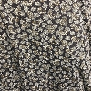 May include: A brown fabric with a white paisley pattern. The fabric has a subtle texture and a slightly wrinkled appearance.