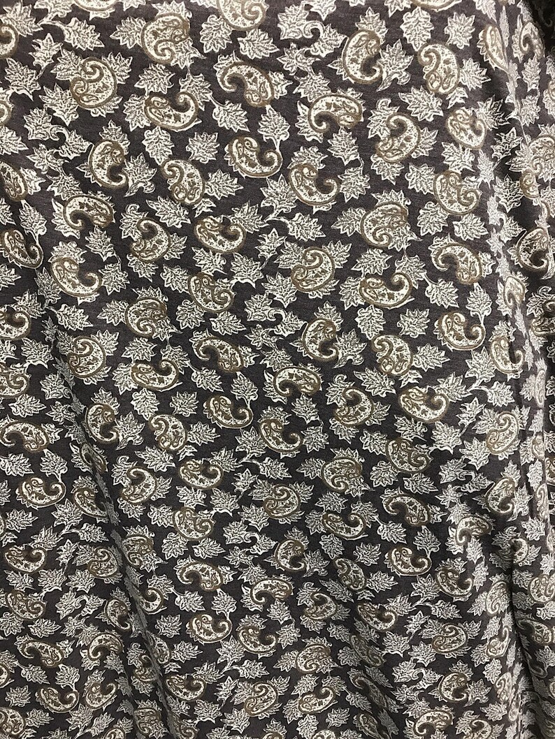 May include: A brown fabric with a white paisley pattern. The fabric has a subtle texture and a slightly wrinkled appearance.