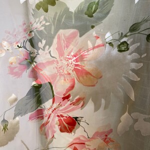 May include: A sheer white fabric with a floral pattern. The flowers are pink, red, and green. The fabric is translucent and has a delicate texture.