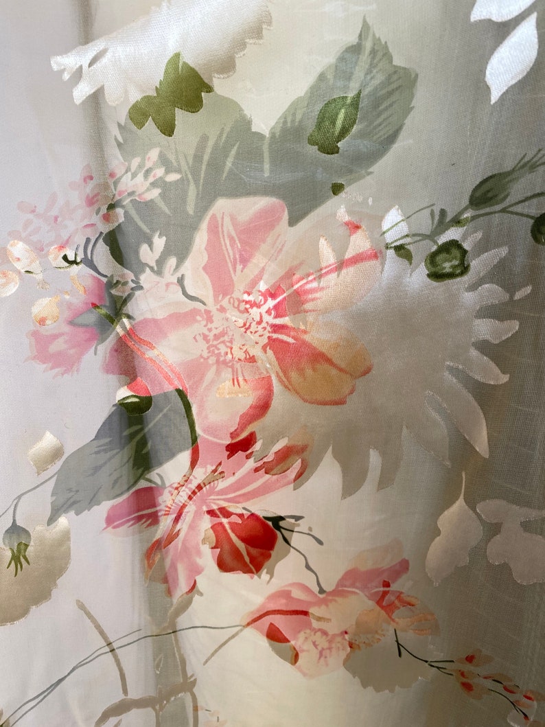 May include: A sheer white fabric with a floral pattern. The flowers are pink, red, and green. The fabric is translucent and has a delicate texture.