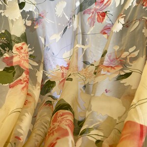 May include: A sheer curtain with a floral pattern in shades of pink, green, and white. The fabric is translucent and the flowers are delicate and intricate.