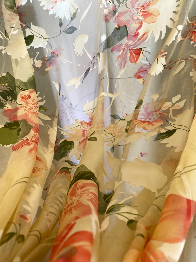 May include: A sheer curtain with a floral pattern in shades of pink, green, and white. The fabric is translucent and the flowers are delicate and intricate.