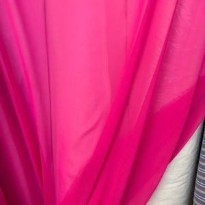 Op de afbeelding: Een helder roze, doorschijnende stof met een gladde textuur. De stof is gevouwen en gedrapeerd, wat de vloeiende aard laat zien.