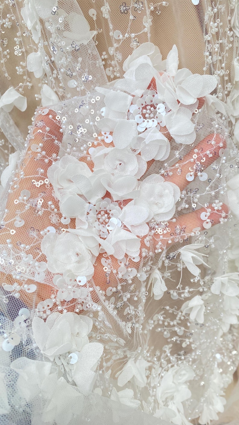 Peut inclure: Tissu de dentelle florale blanche avec des embellissements de fleurs 3D et des paillettes.