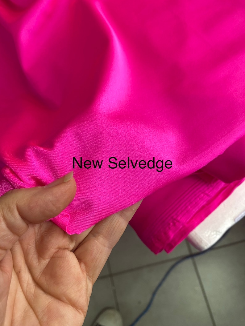 May include: Close-up of a bright pink fabric with a selvedge edge. The fabric is smooth and shiny, and the selvedge edge is visible. The text "New Selvedge" is printed on the fabric.