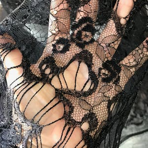 May include: Black lace fabric with a delicate floral pattern. The fabric is sheer and has a soft, flowing texture.